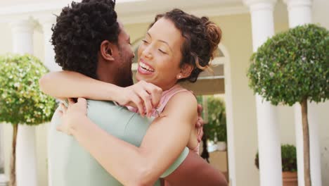 feliz pareja biracial abrazándose con alegría frente a la nueva casa