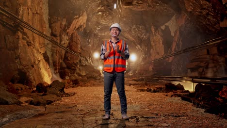 full body of asian male engineer with safety helmet smiling and clapping his hands while standing in underground mine tunnel