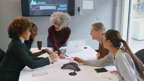 mujer de negocios madura que lidera una reunión creativa de mujeres que colaboran en torno a una mesa en una oficina moderna