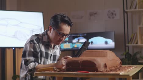 asian man automotive designer celebrating success following a tablet working on the sculpture of car clay by rake or wire in the studio