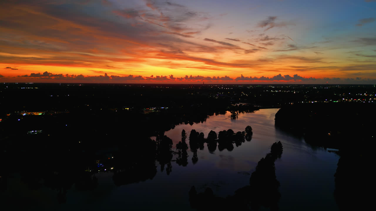 Fiery sunset over a still lake with vivid reflections, deep orange and red sky dominates, aerial slow fly forward, space for text at center