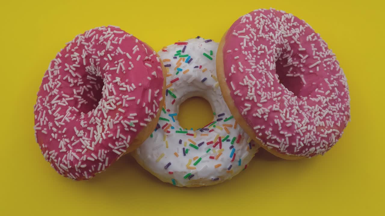 girando un primer plano de rosas y blancas sabrosas y deliciosas rosquillas dulces con salpicaduras coloridas sobre un fondo amarillo.