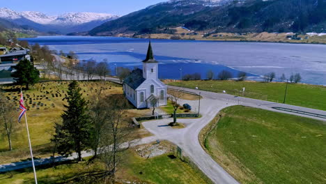 aerial view of norweigan church next to river and mountains