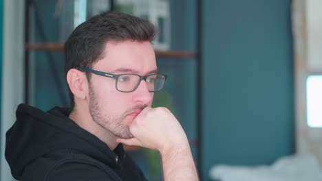 Pensive-young-man-sitting-pondering-in-living-room