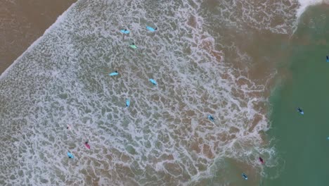 Top-down-rotating-aerial-of-waves-crashing-on-longboard-surfers-at-sandy-beach