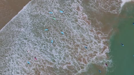 arriba abajo antena giratoria de las olas que se estrellan en los surfistas de longboard en la playa de arena