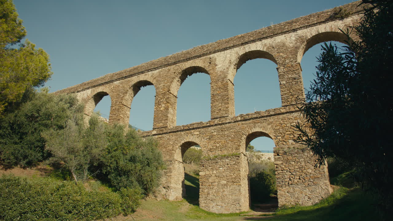 Historic aqueduct with tall arches made of stone stretches through lush countryside, showcasing Roman-style engineering and timeless beauty