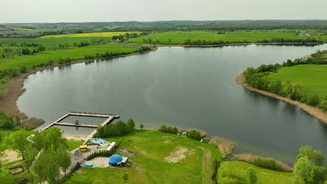 Wielochowskie-See---Blick-Auf-Einen-Ruhigen-See,-Umgeben-Von-Dichtem-Laubwerk,-Mit-Angrenzenden-Weitläufigen-Gelben-Rapsfeldern,-Die-Den-Himmel-Reflektieren-Und-Eine-Friedliche-Und-Reflektierende-Naturlandschaft-Schaffen