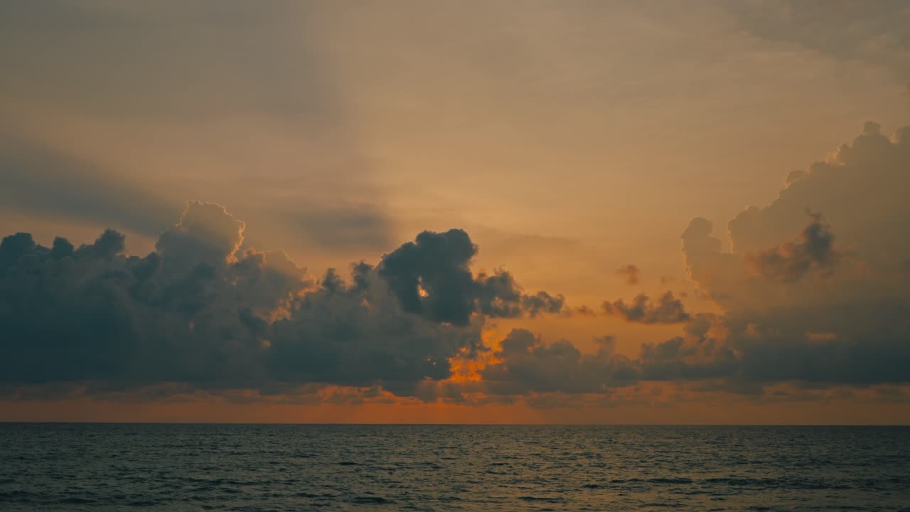 Yellow and orange sunset sky above a calm ocean with dramatic clouds and crepuscular rays shining through. Scenic seascape with glowing light beams and peaceful evening atmosphere