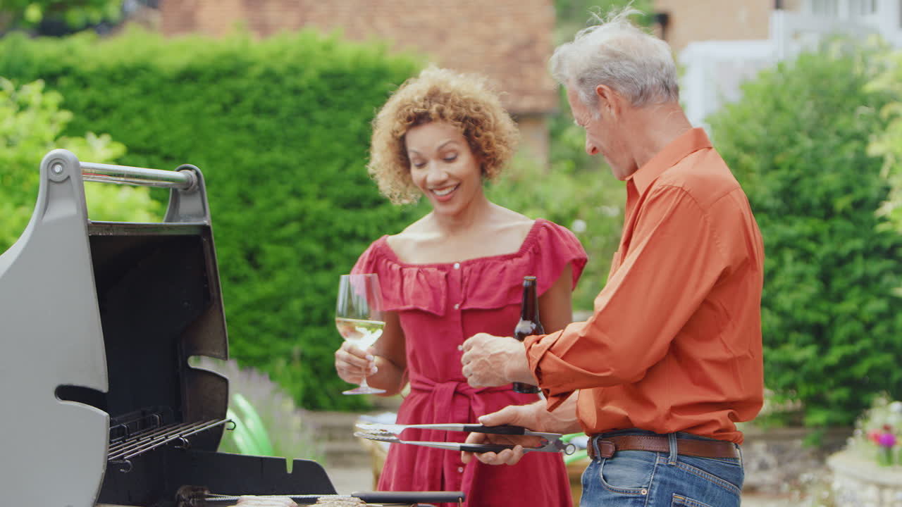 Coppia anziana che cucina un barbecue all'aperto e beve vino e birra a casa.