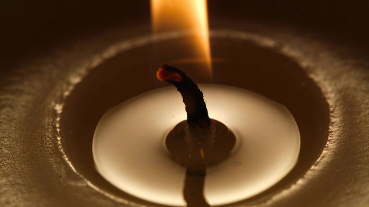Camera framing candle wick, textured rim and wax pool in low-light, flame flickering for warm light
