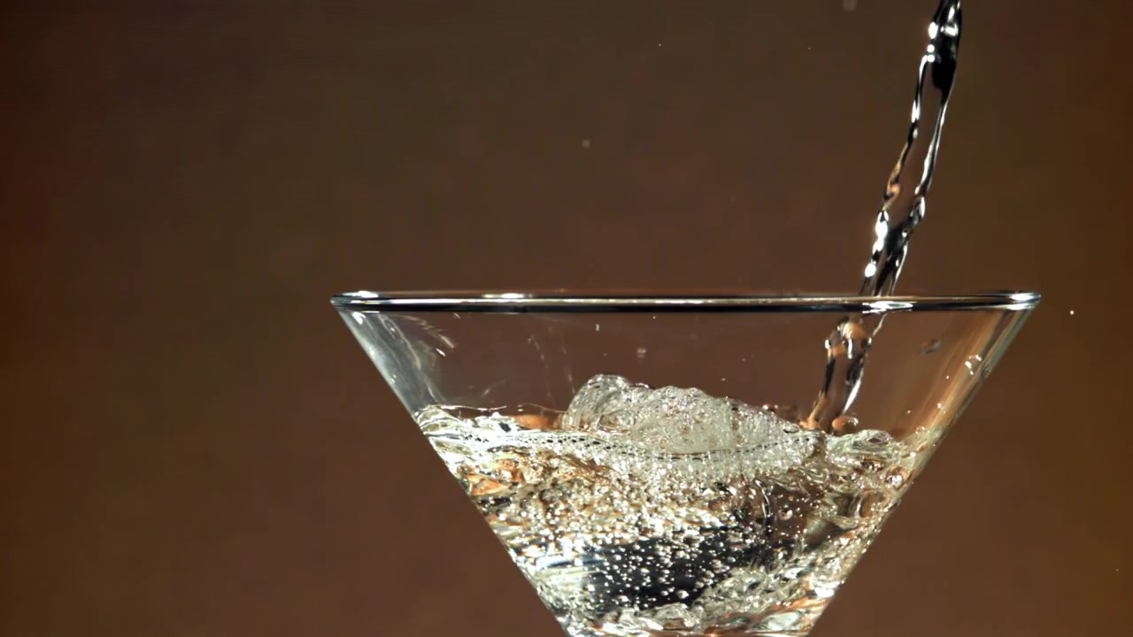 Liquido trasparente versato in un bicchiere da Martini al rallentatore
