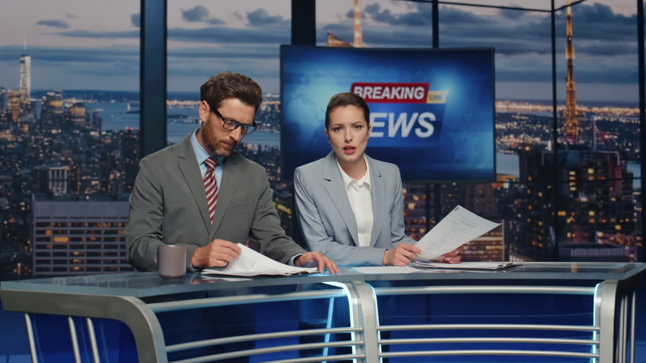 Primer plano de presentadores destacando noticias de última hora en estudio de televisión nocturno. Los anclas discuten.