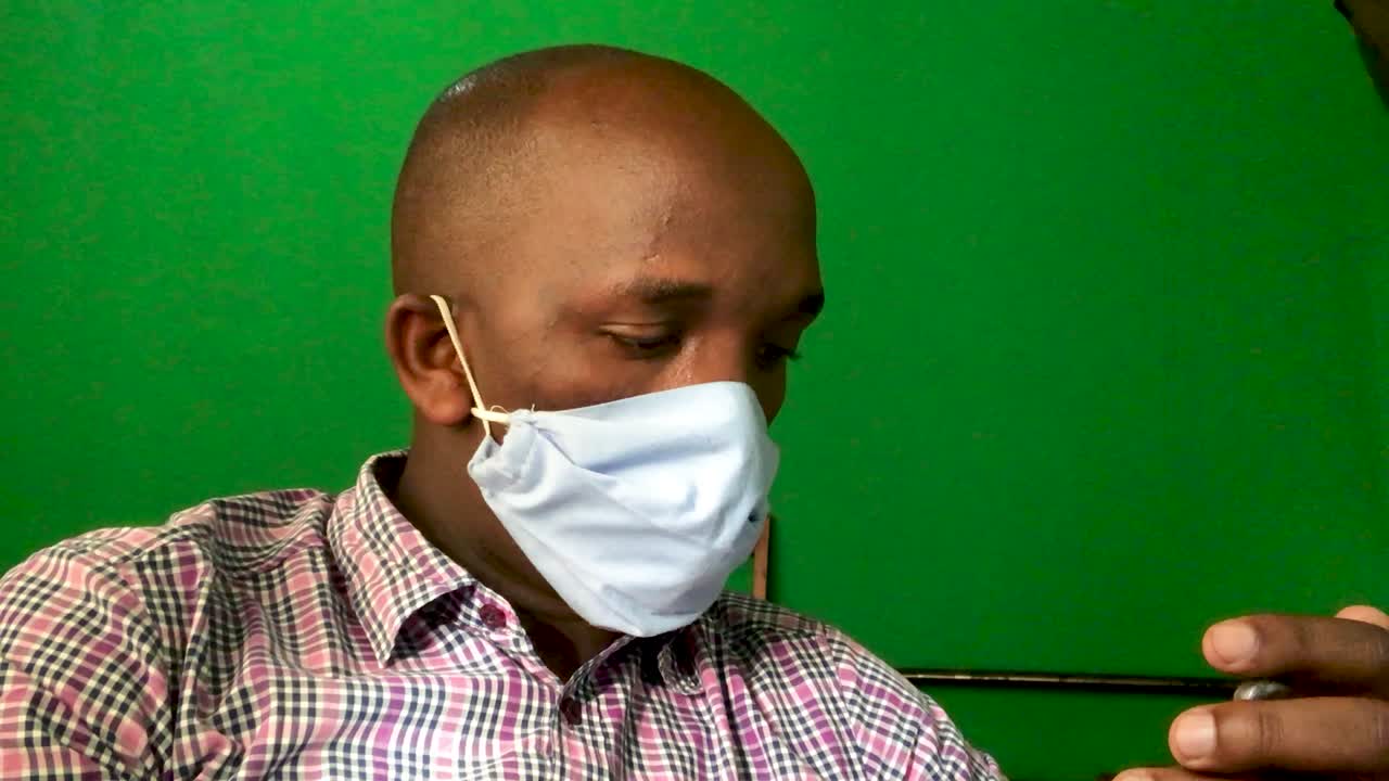 Uomo dalla pelle scura che indossa una mascherina e controlla il suo smartphone durante la quarantena a casa. Pandemia di Covid-19 in tutto il mondo. Schermo verde sullo sfondo.