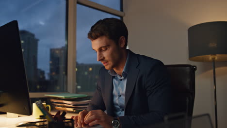 man workaholic staying late in dark office. smiling manager analysing papers