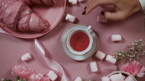 Draufsicht-Auf-Eine-Person,-Die-Eine-Tasse-Tee-Auf-Einem-Rosafarbenen-Tisch-Trinkt