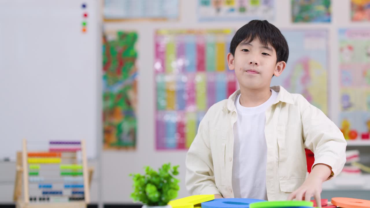 Young boy smiles and holds foam number two in brightly lit classroom, cheerful educational environment