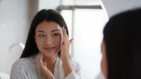 woman applying skincare in bathroom mirror