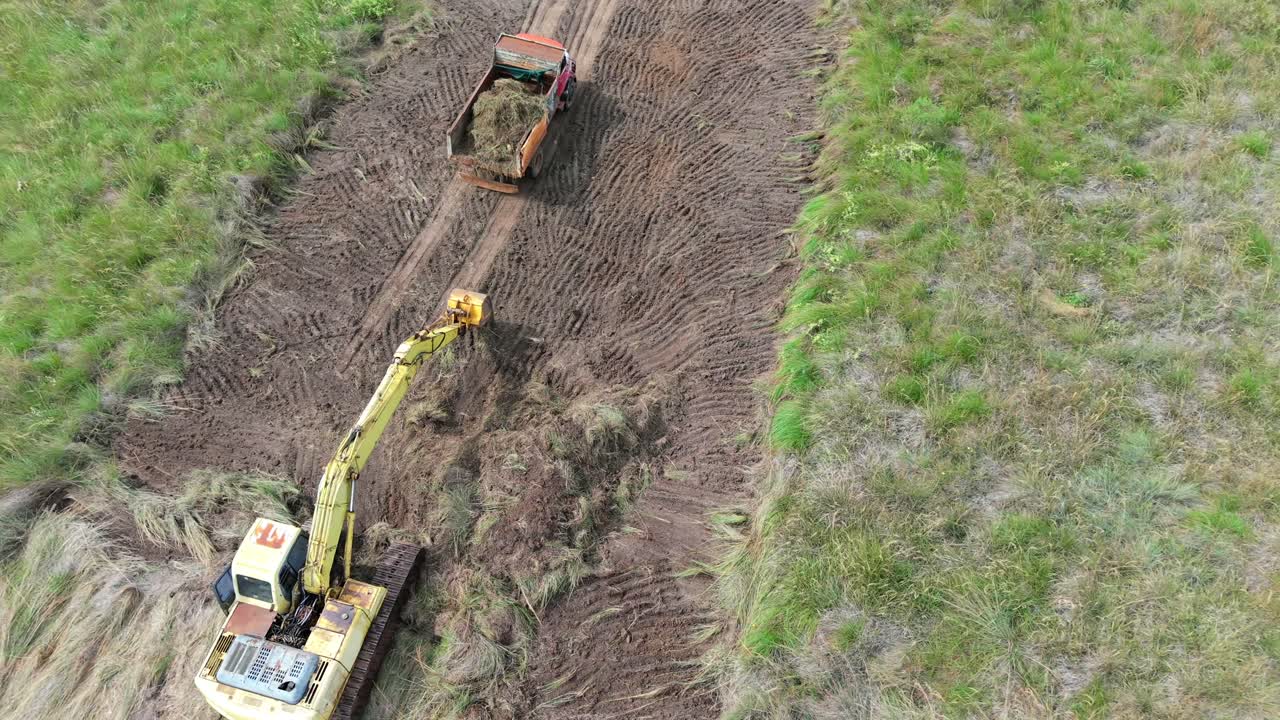 Excavator machine and truck working in narrow dirt track for earthmoving.