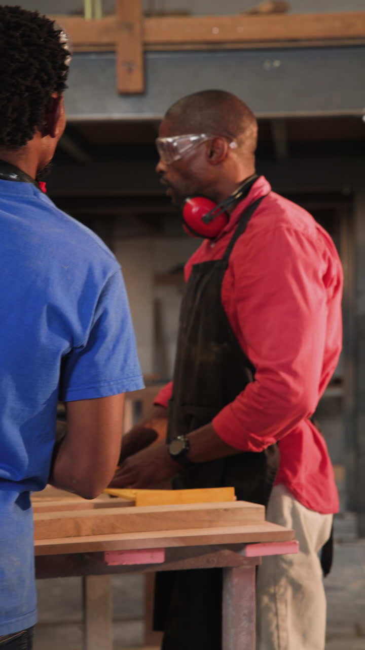Vertical video: African American mentor measuring board guiding apprentice assembling frame at shop