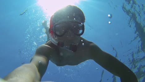 enthusiastic male scuba diver with red snorkel diving down the blue sea water, going deep without breath in slowmo