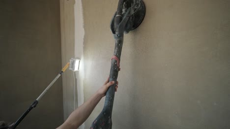 worker using a pole sander to smooth a wall surface during the drywall finishing phase of interior construction