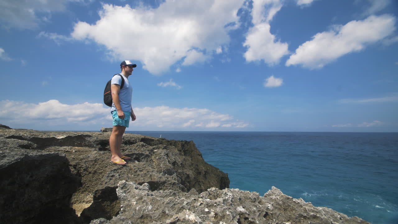 hombre viajero parado en el borde de las rocas mirando al océano
