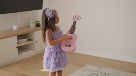 a beautiful little girl is playing the ukulele in the living room for her mom.