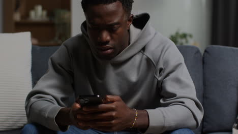 close up of unhappy and depressed young man sitting on sofa at home looking at mobile phone 4