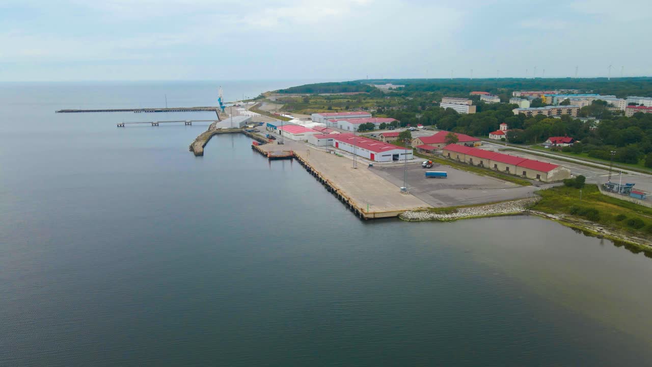 Aerial drone footage of a empty international trading cargo harbor or port at a cloudy day in Paldiski Pakri, where large warehouses and cranes are waiting for shipments. Local apartment buildings too