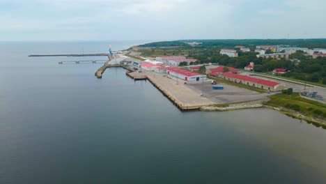 aerial drone footage of a empty international trading cargo harbor or port at a cloudy day in paldiski pakri, where large warehouses and cranes are waiting for shipments. local apartment buildings too