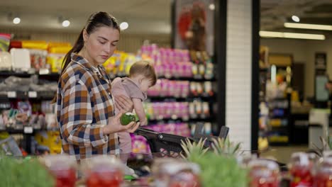 A-brunette-woman-in-a-plaid-shirt-with-her-little-daughter-in-her-arms-chooses-fruits-in-the-supermarket-department