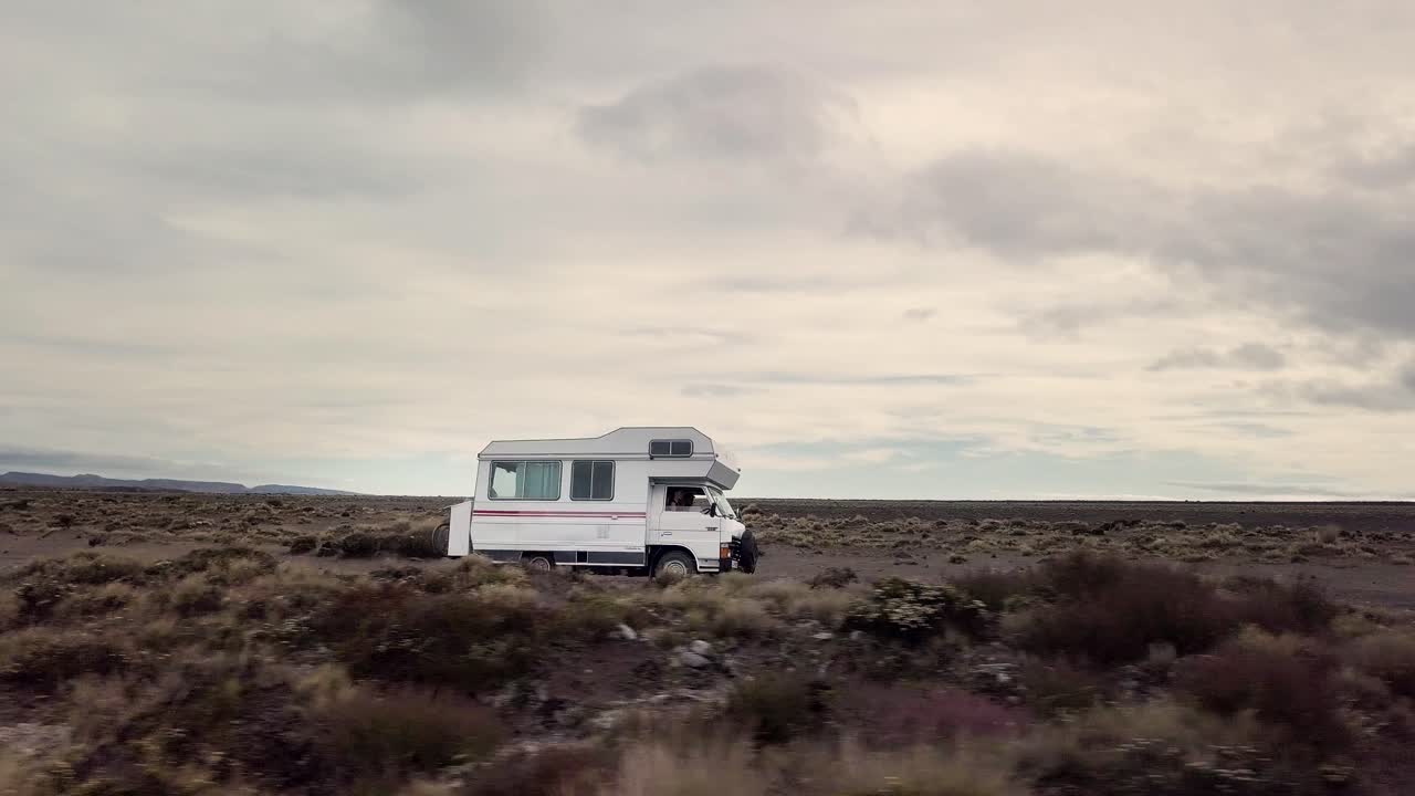 An old camper van drives through the desert at Tukino Access Road, Tongariro National Park - Rangipo Desert. Its a cloudy day.