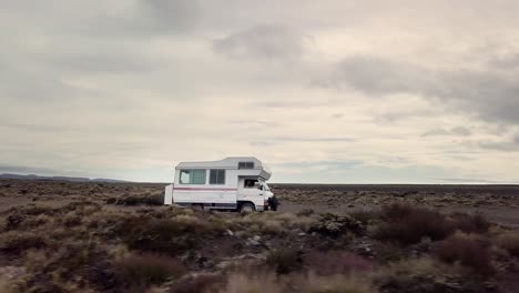 an old camper van drives through the desert at tukino access road, tongariro national park - rangipo desert. its a cloudy day.