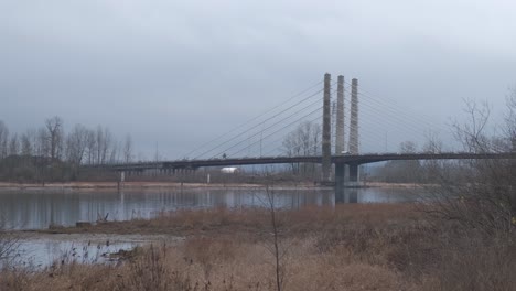 local traffic on a bridge over a blue river with bare trees and fallen leaves on a cloudy day