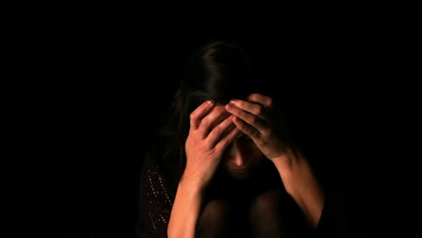 upset brunette with head in hands on black background