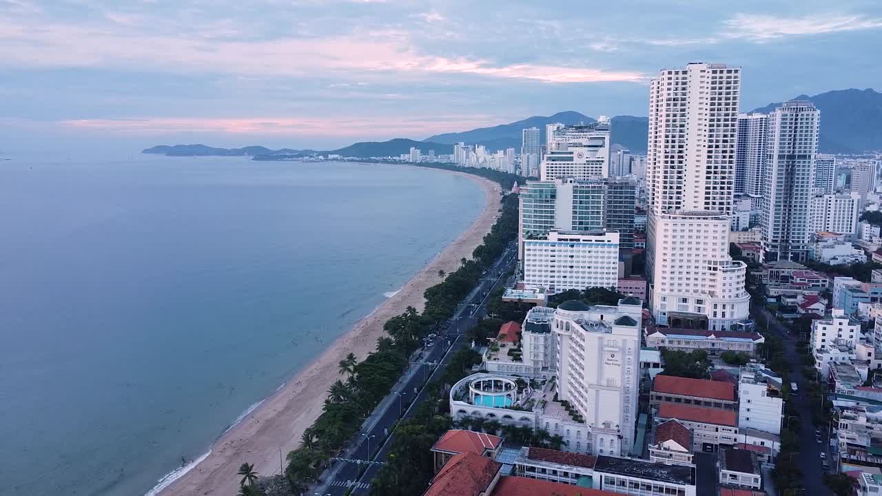 Drone video captures vibrant fishing boats clustered on Da Nang's turquoise waters, near sandy beach. Coastal townscape visible under clear skies, adding a picturesque charm