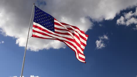 united states flag in the wind with blue sky background with clouds