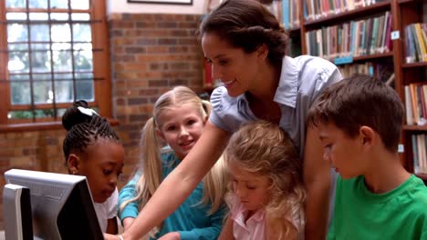 Pretty-teacher-using-computer-with-pupils-in-library