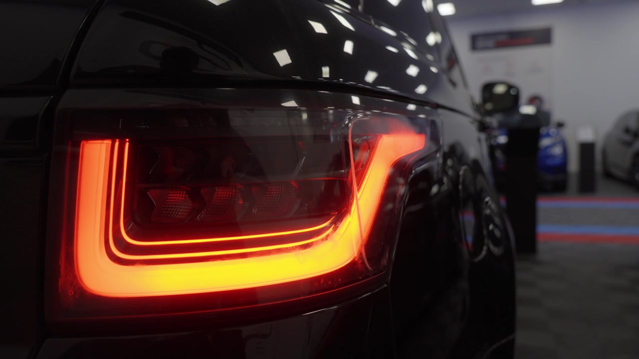 Fanale posteriore a LED arancione di un SUV di lusso moderno che lampeggia all'avvio dell'auto, primo piano. Design automobilistico premium su carrozzeria nera lucida in showroom.