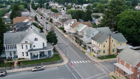 establishing shot, aerial of anytown usa, small town in america with american flag flying, united states community neighborhood homes, historic colonial houses line street as traffic passes by, summer