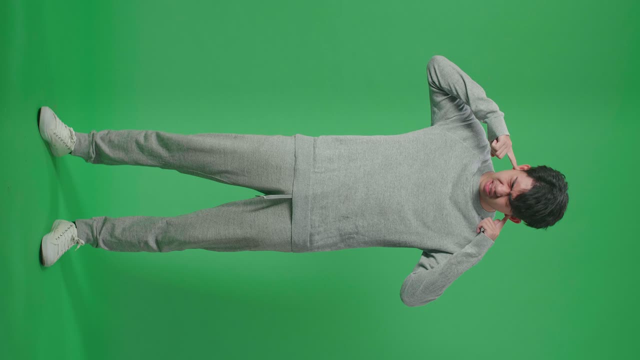 Full Body Of Stressed Asian Man Covering Her Ears While Standing In Front Of Green Screen Background