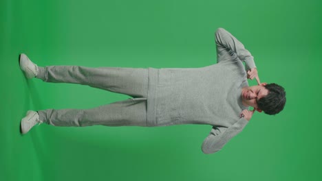 full body of stressed asian man covering her ears while standing in front of green screen background