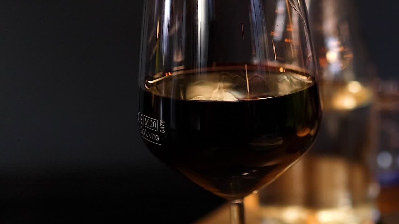 Un primo piano di vino rosso che si mescola delicatamente in un bicchiere sotto una luce soffusa e intensa