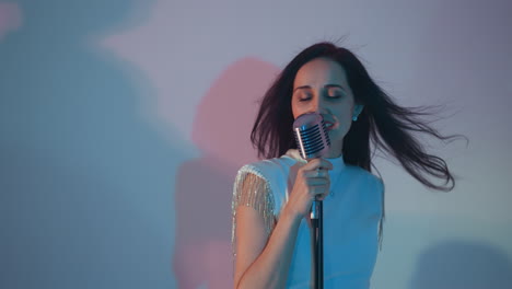 a singer in a white dress passionately sings, holding a vintage microphone with one hand against a blue background. her hair flows back