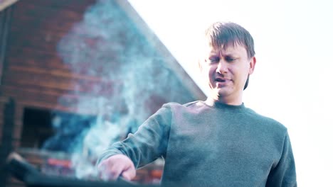 Close-up-Young-man-standing-near-the-summer-house-prepares-the-coals-in-the-grill-stirs-them-with-a-stick