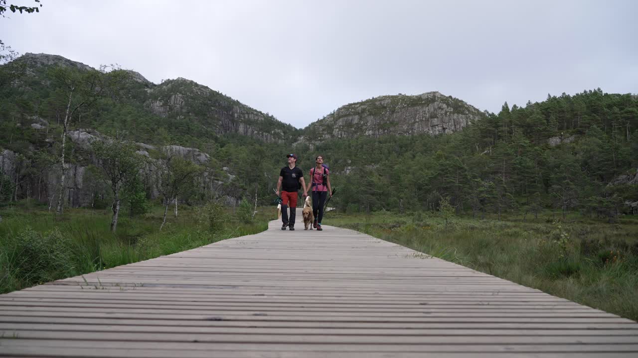 Couple walking with dog on a wooden path in scenic Norwegian nature