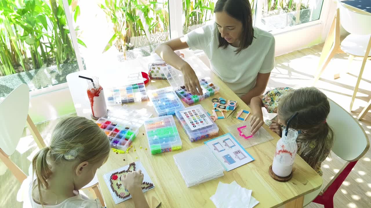 madre e hijas haciendo artesanía de cuentas en un café