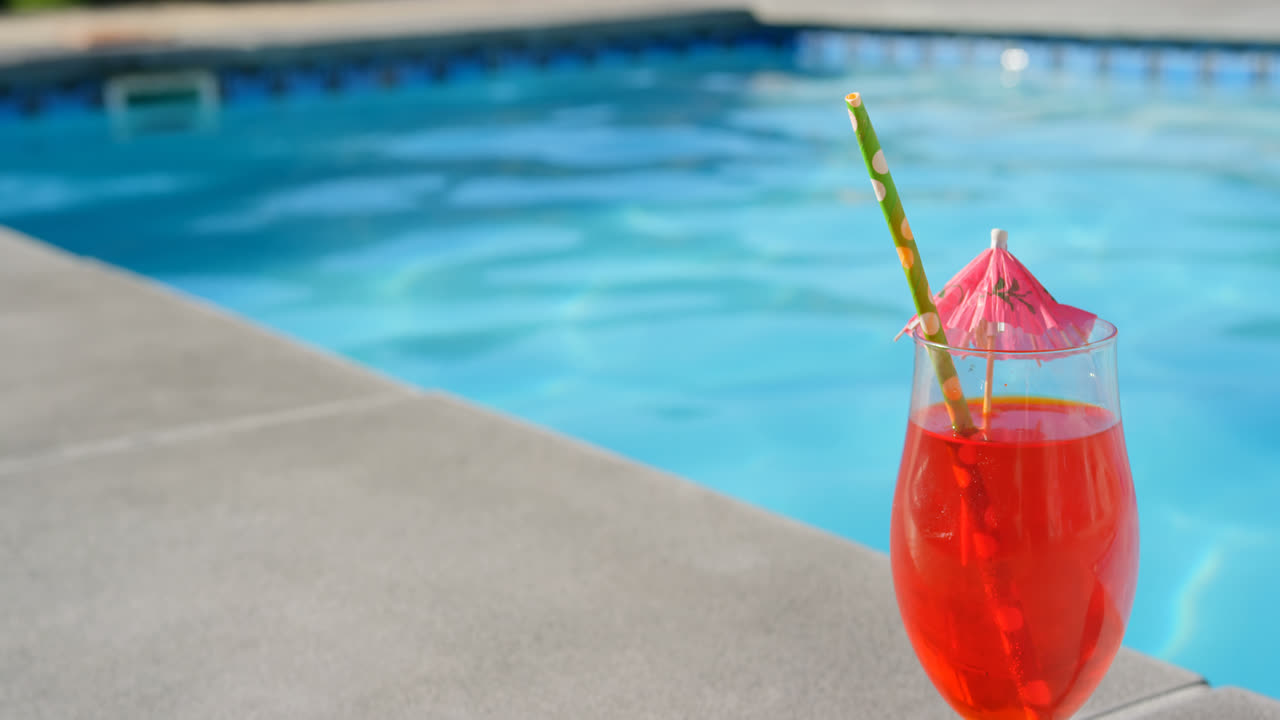 Nahaufnahme eines Cocktailglases mit Schirm und Strohhalm in der Nähe eines Schwimmbads 4k.