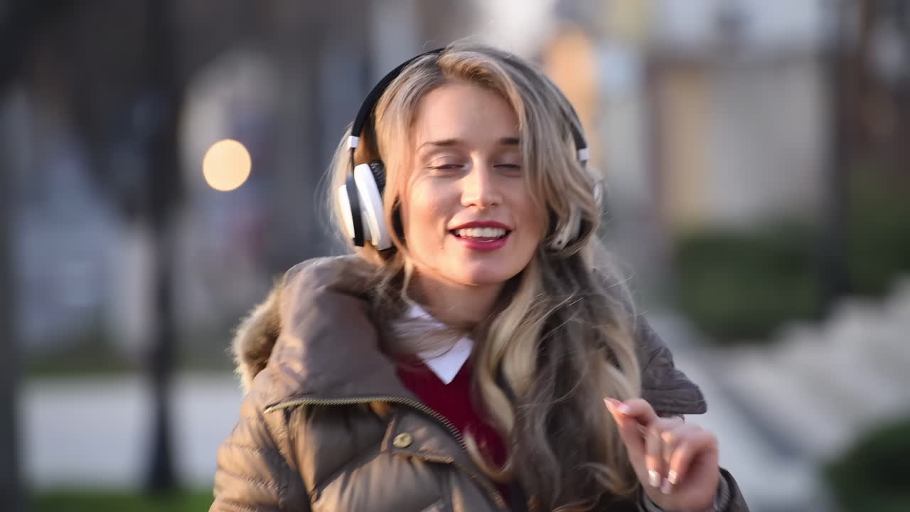 Woman listening to music in her headphones while singing along and dancing in the street